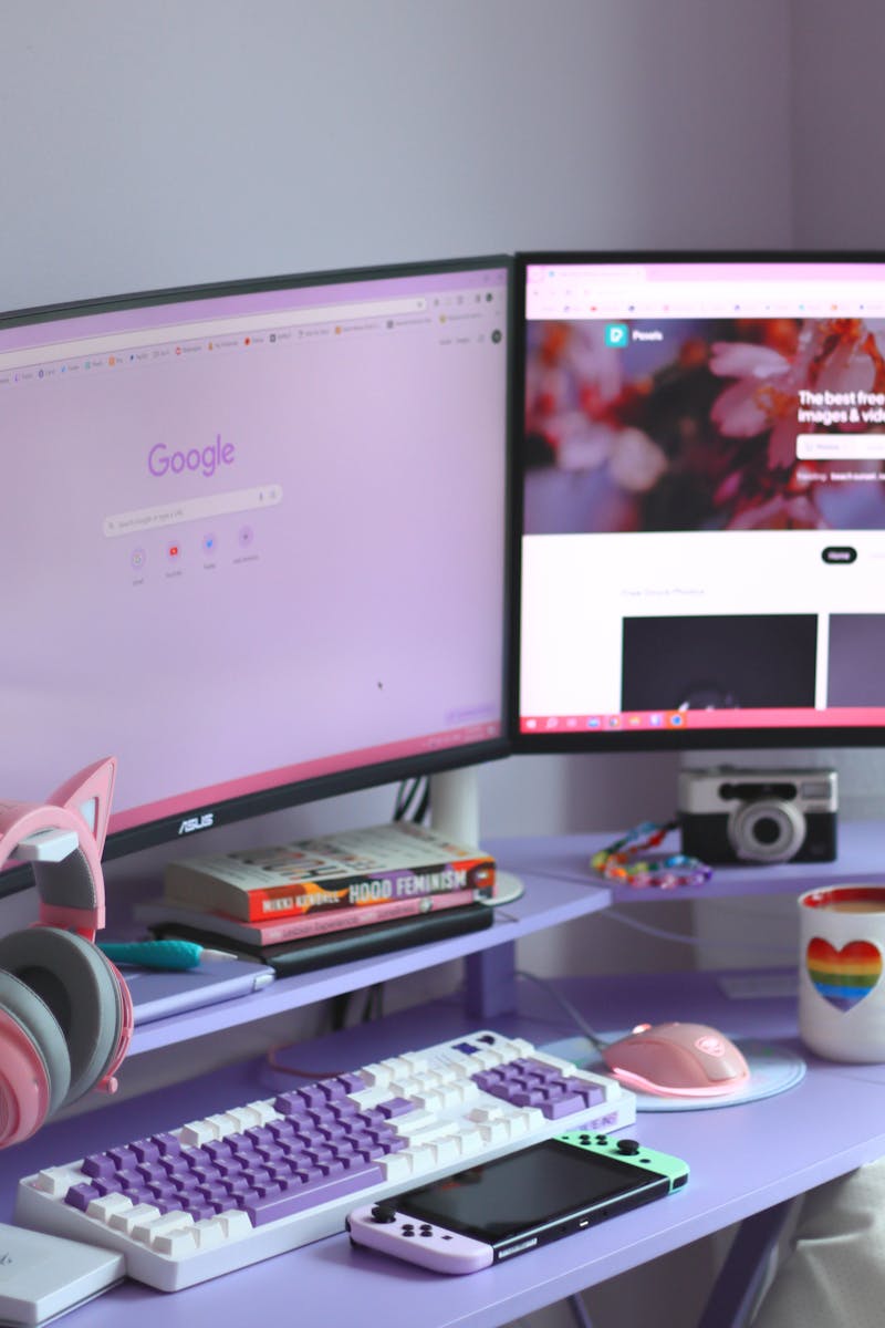 Stylish desk setup with dual monitors, keyboard, headphones, and cozy decor for tech enthusiasts.